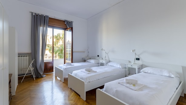A hotel room with three single beds, a wooden floor, a window with curtains, and a view of the outside. - JOIVY Apt For 7 Perfect For Families Close To Beaches (Genoa)