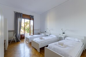 A hotel room with three single beds, a wooden floor, a window with curtains, and a view of the outside. - JOIVY Apt For 7 Perfect For Families Close To Beaches (Genoa)