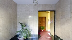 A hallway with marble walls, a potted plant, and a red carpet leading to a wooden door. - JOIVY Apt For 7 Perfect For Families Close To Beaches (Genoa)
