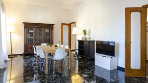 A dining area with a marble floor, a wooden cabinet, a television, and a door. - JOIVY Apt For 7 Perfect For Families Close To Beaches (Genoa)