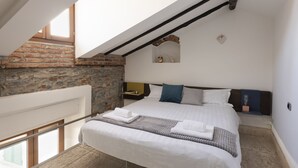 A bedroom with a sloped ceiling, exposed brick wall, and a bed with white linens and a gray throw blanket. - JOIVY Cosy Apt in Como Centre (Como)