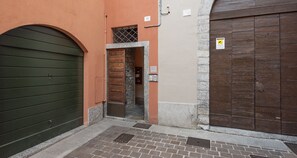 A narrow alleyway with a green shutter door, a stone entrance, and a brown wooden door. - JOIVY Cosy Apt in Como Centre (Como)