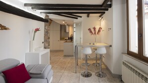 A modern kitchen with a central island, a dining area with bar stools, and a view of the street through a large window. - JOIVY Cosy Apt in Como Centre (Como)