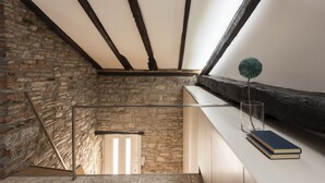 A staircase with a stone wall on one side and a wooden beam ceiling. A glass vase with a green spherical object and two books are on a ledge. - JOIVY Cosy Apt in Como Centre (Como)