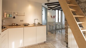 A modern kitchen with white cabinets, a wooden countertop, and a built-in sink. There is a stone wall and a wooden staircase leading to another room. - JOIVY Cosy Apt in Como Centre (Como)