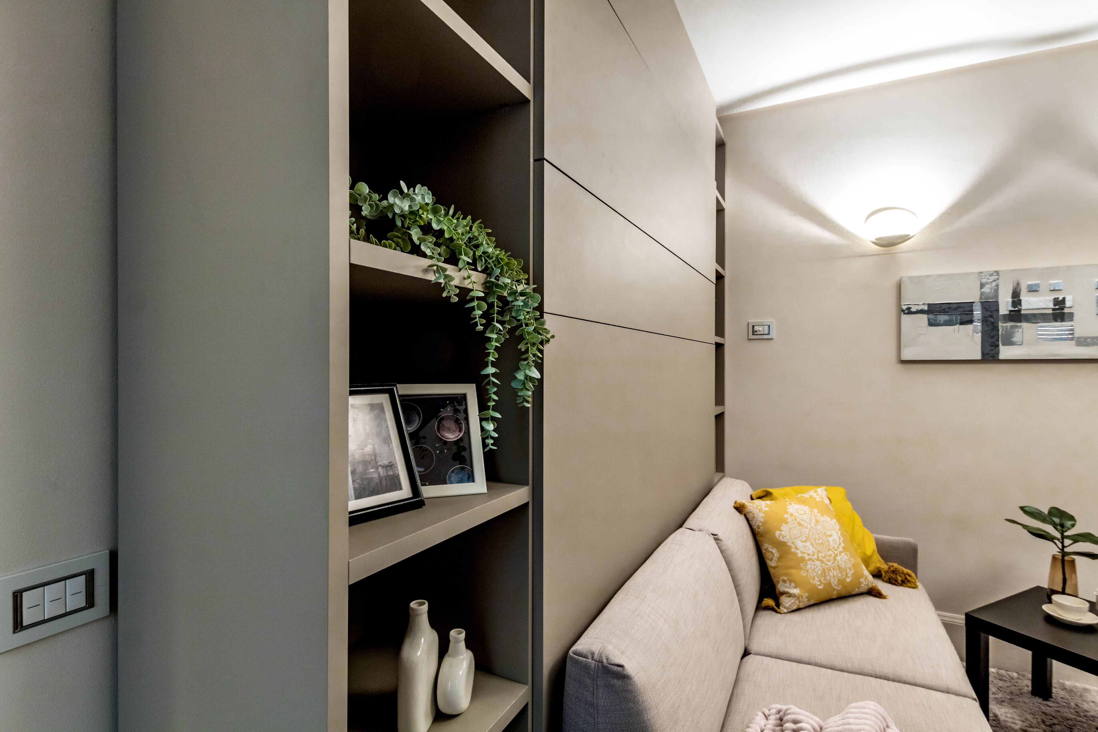 A modern living room with a sofa, a small table, and a shelf with decorative items.
