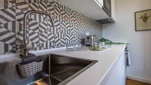 A modern kitchen with a geometric patterned backsplash, a stainless steel sink, and a white countertop.
