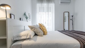 A neatly made bed with a white and patterned pillow arrangement, a bedside lamp, and a large mirror on the wall.