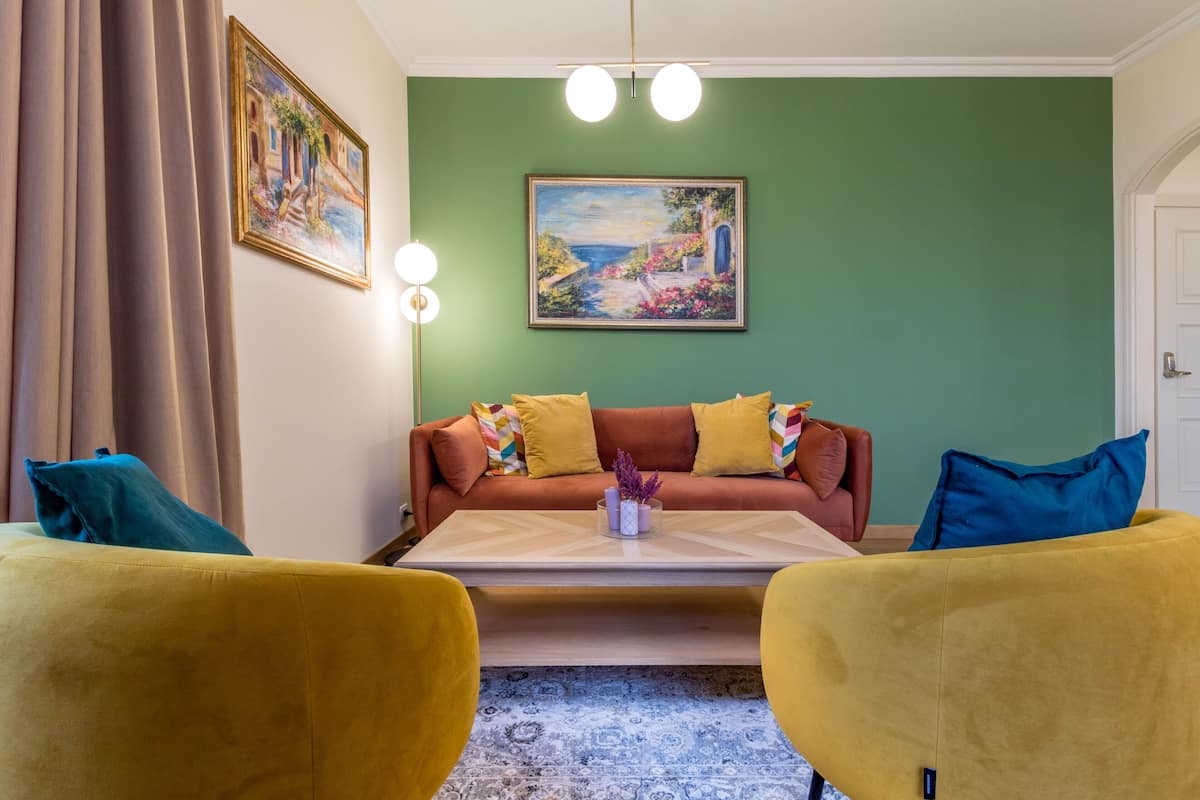 Uma sala de estar com sofá, duas poltronas amarelas, mesa de centro e um quadro na parede.