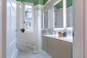 A bathroom with a glass-enclosed shower, a sink with a marble countertop, and a mirror above the sink.