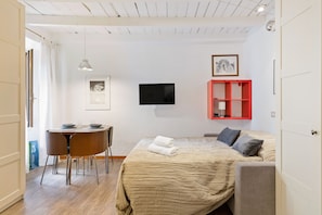 A bedroom with a bed, a TV, a dining table with chairs, and a red shelf unit.
