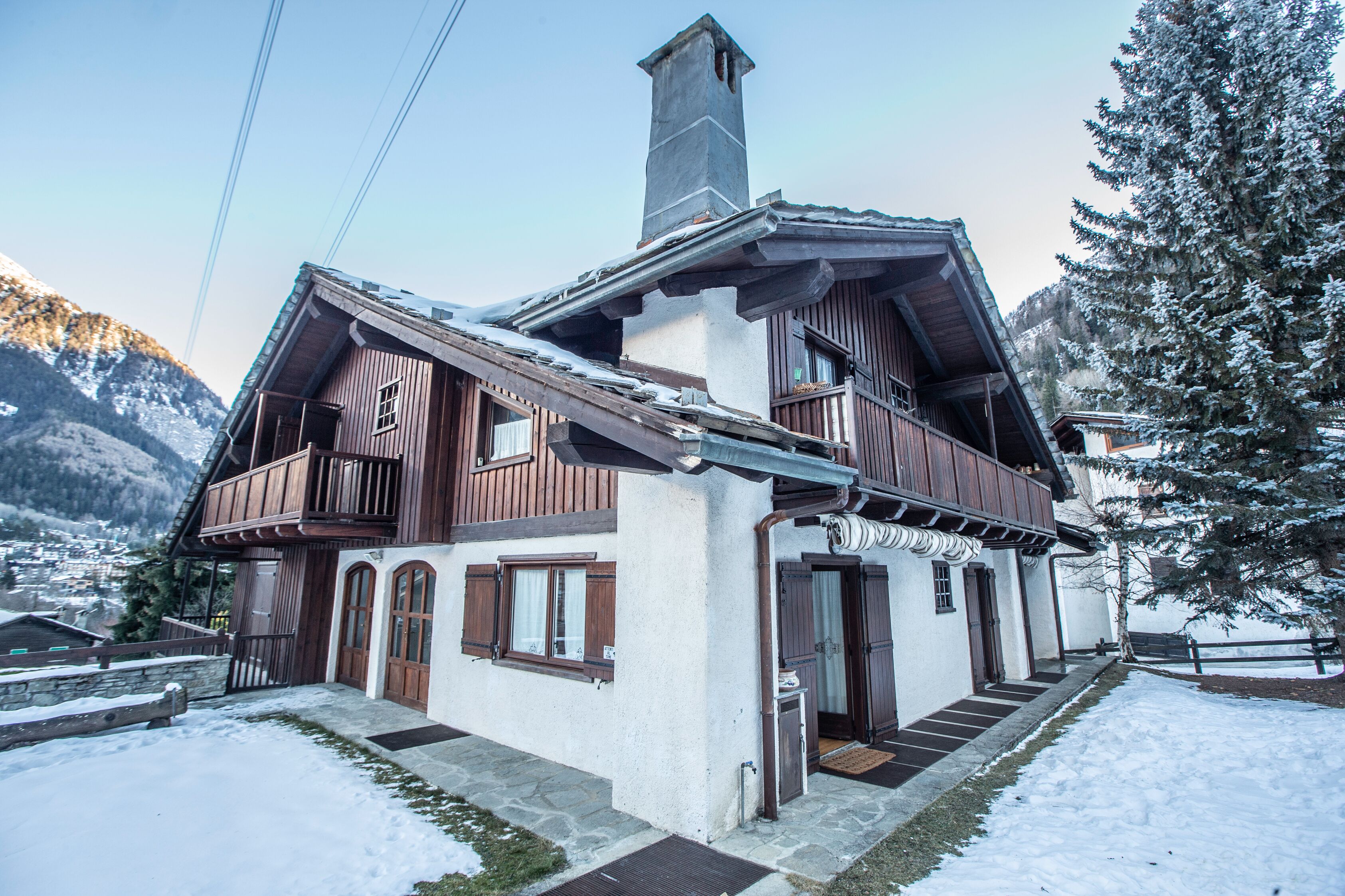 Eine zweistöckige Holzchalet mit Balkon, vor einer verschneiten Berglandschaft.
