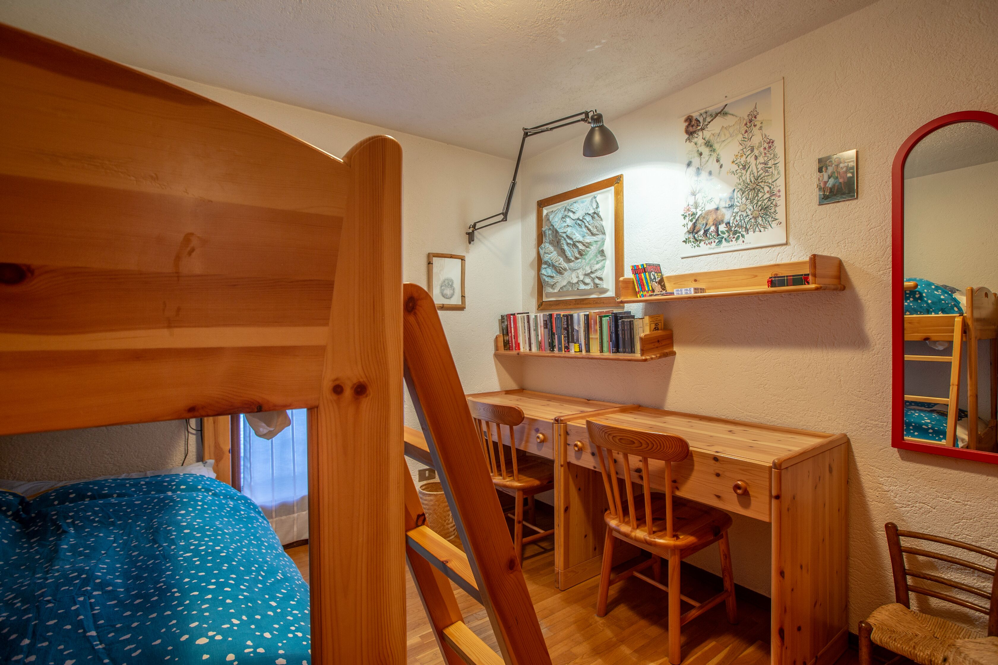 Ein Schlafzimmer mit einem Holzbett, einem Schreibtisch mit Stuhl, einem Bücherregal und einem Spiegel.