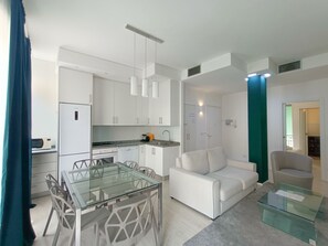 A modern kitchen with white cabinets, a glass dining table, and a white sofa.