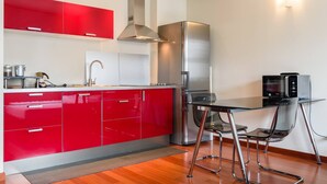 A modern kitchen with red cabinets, stainless steel appliances, and a glass dining table with metal chairs. - JOIVY Bright Studio For 2 Close To Milano Centrale (Milan)