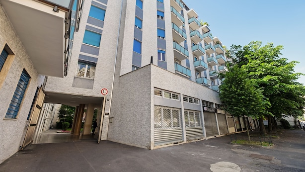 A multi-story residential building with balconies, a garage entrance, and a tree in the foreground. - JOIVY Lovely Flat For 4 W/Balcony Near Porta Romana (Milan)