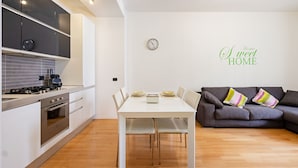 A modern kitchen with a dining area, a gray sofa, and a wall clock. - JOIVY Lovely Flat For 4 W/Balcony Near Porta Romana (Milan)
