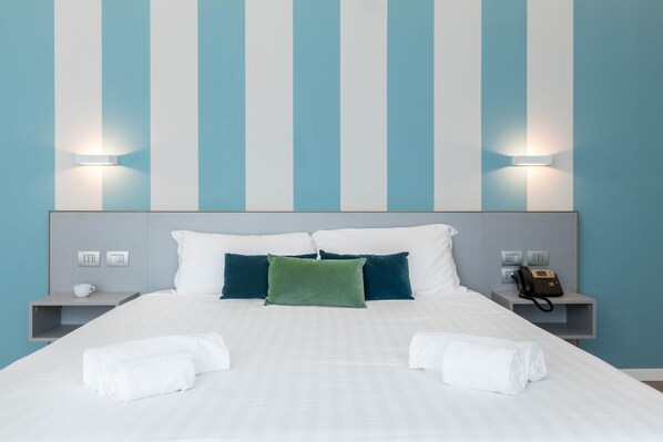 A hotel room with a large bed, two pillows, a bedside table with a phone, and wall-mounted lights. - JOIVY San Cristoforo - Terrace, Gym & SPA (Milan)