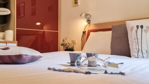 Un letto rifatto con cura, un servizio da tè, cuscini e una lampada da comodino in una camera d'albergo.