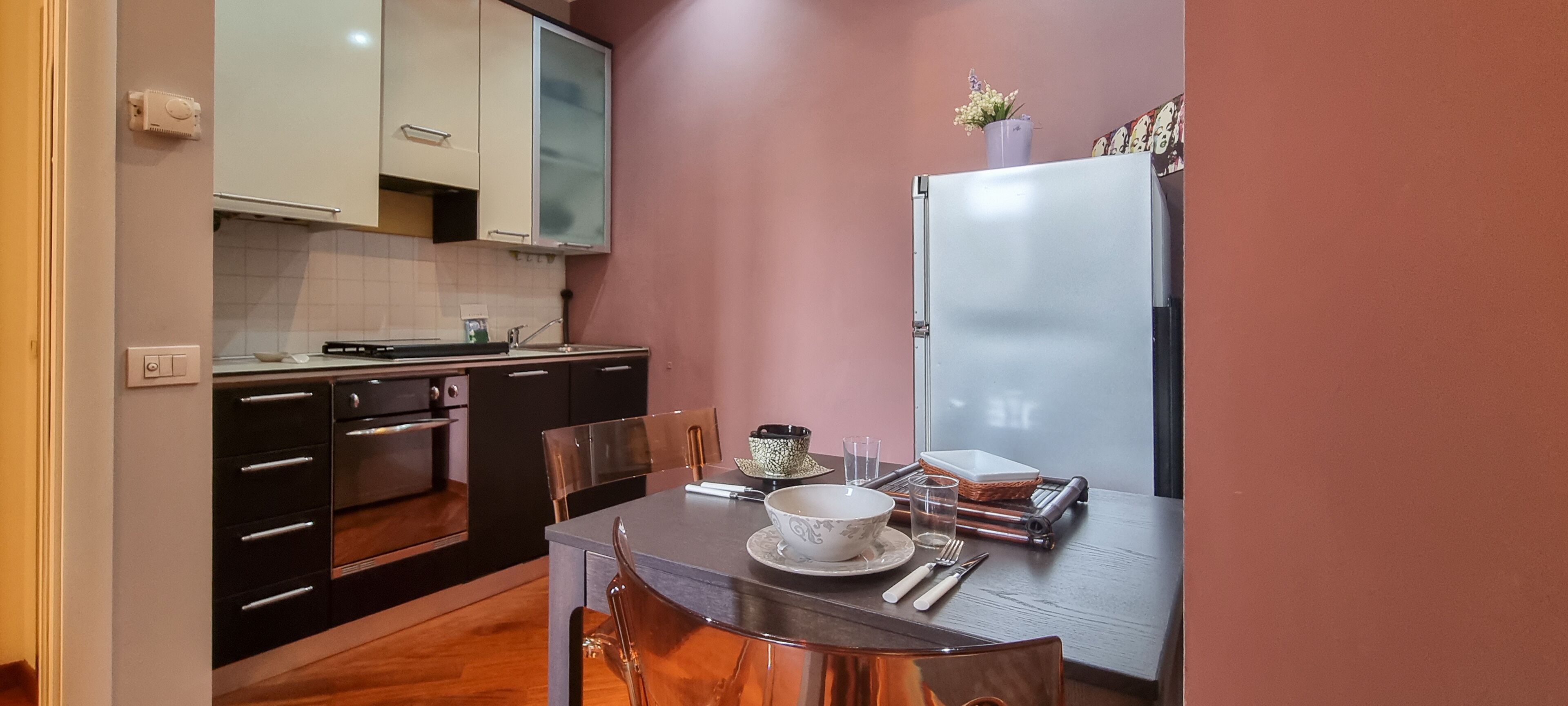 A compact kitchen with a dining table set for two, featuring a bowl, glass, and cutlery.