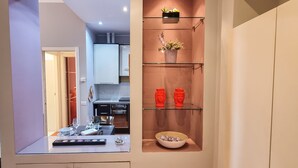 Una cucina moderna con un divisorio in vetro, una zona pranzo con un tavolo apparecchiato per due e uno scaffale decorativo con vasi e una ciotola.