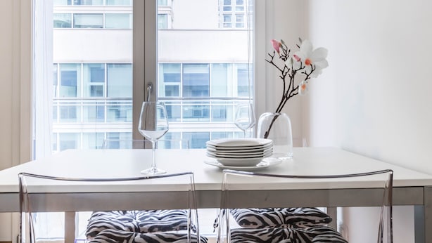 A dining table with a vase of flowers, a stack of plates, and wine glasses.