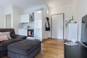 Eine moderne Wohnung mit grauem Sofa, Pouf in Schwarz, einer Küche mit weißen Schränken und Holzboden.