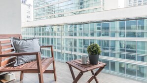 A balcony with a wooden bench, a small table, and a potted plant.