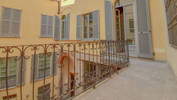 Un bâtiment doté de nombreuses fenêtres, dont certaines sont pourvues de volets, et d’un balcon orné de rampes en métal ouvragé.