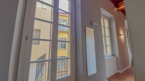 Un couloir doté de grandes fenêtres en arc de cercle, d’un plancher en bois et offrant une vue sur un immeuble jaune avec des balcons.