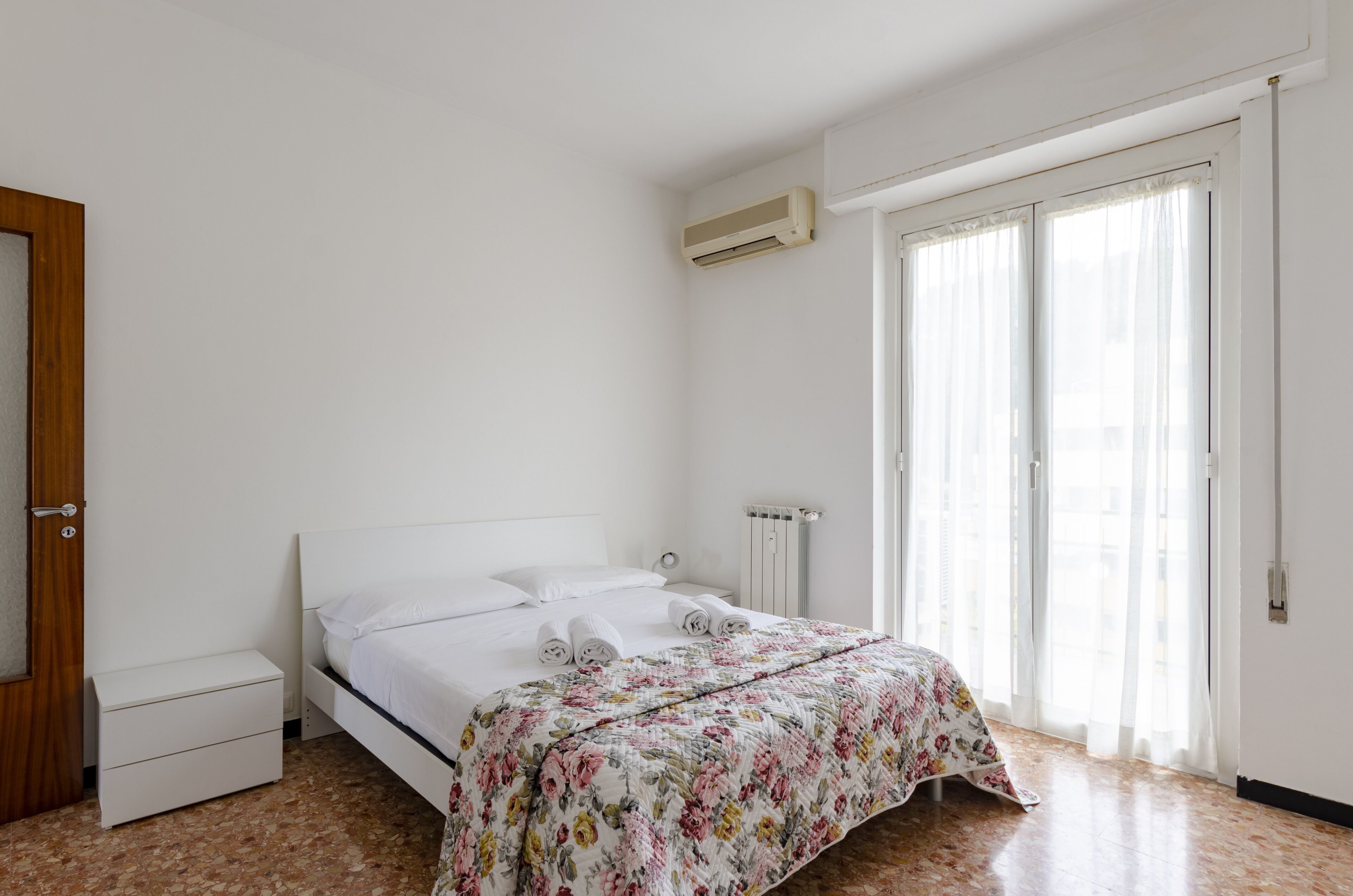 A bedroom with a bed, a nightstand, a radiator, and a window with curtains.