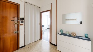 A hallway with a wooden door, a white sliding door, and a white cabinet with a mirror and small items on top. - JOIVY Family Flat W/Terrace & Parking Near Beach (Sestri Levante)