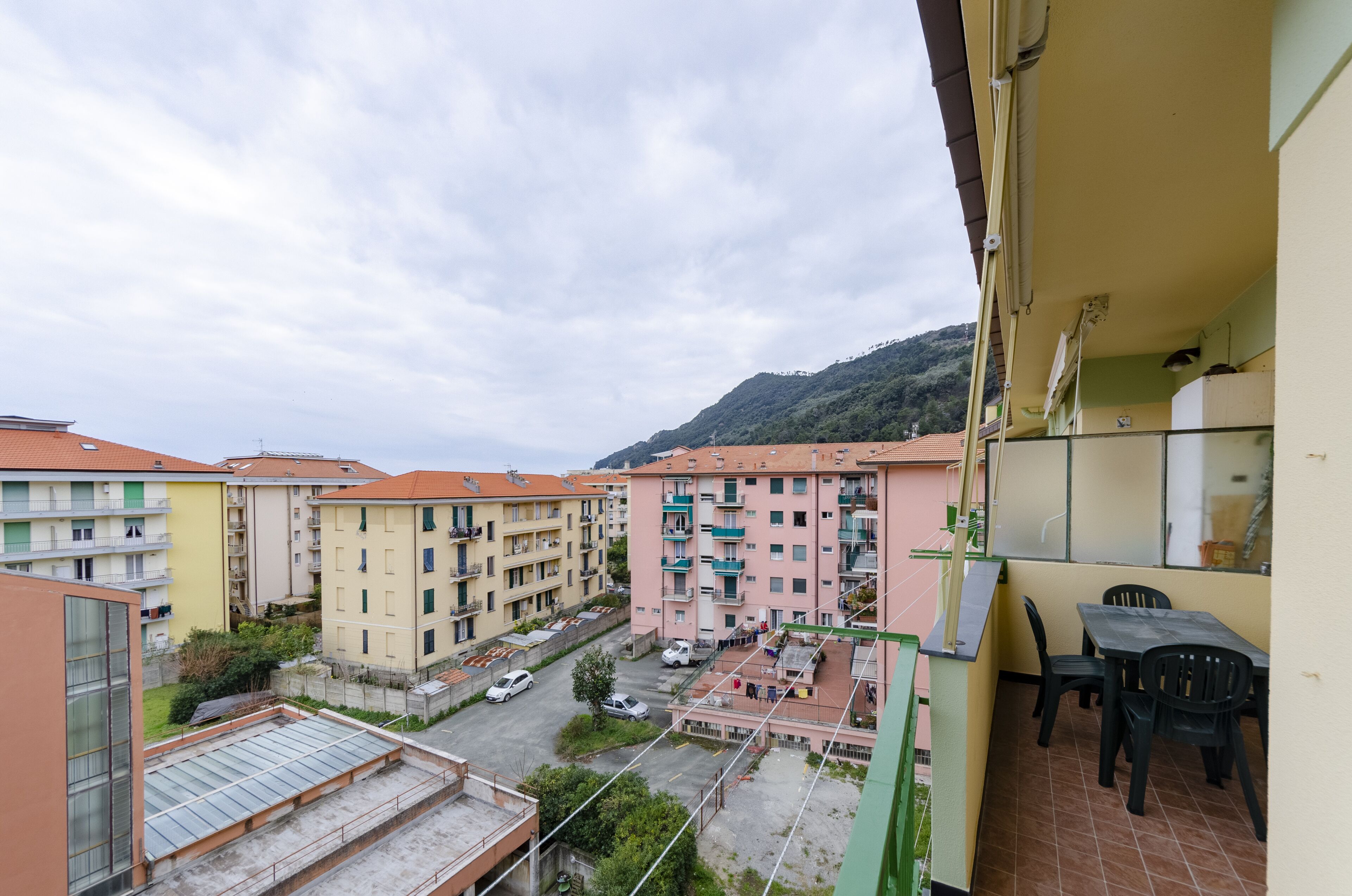 A residential building with multiple balconies, a tiled roof, and a view of a street with parked cars.