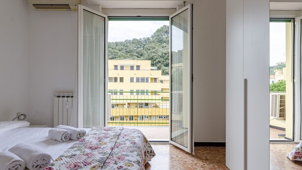 A hotel room with a bed, a window with a view of buildings, and a radiator. - JOIVY Family Flat W/Terrace & Parking Near Beach (Sestri Levante)
