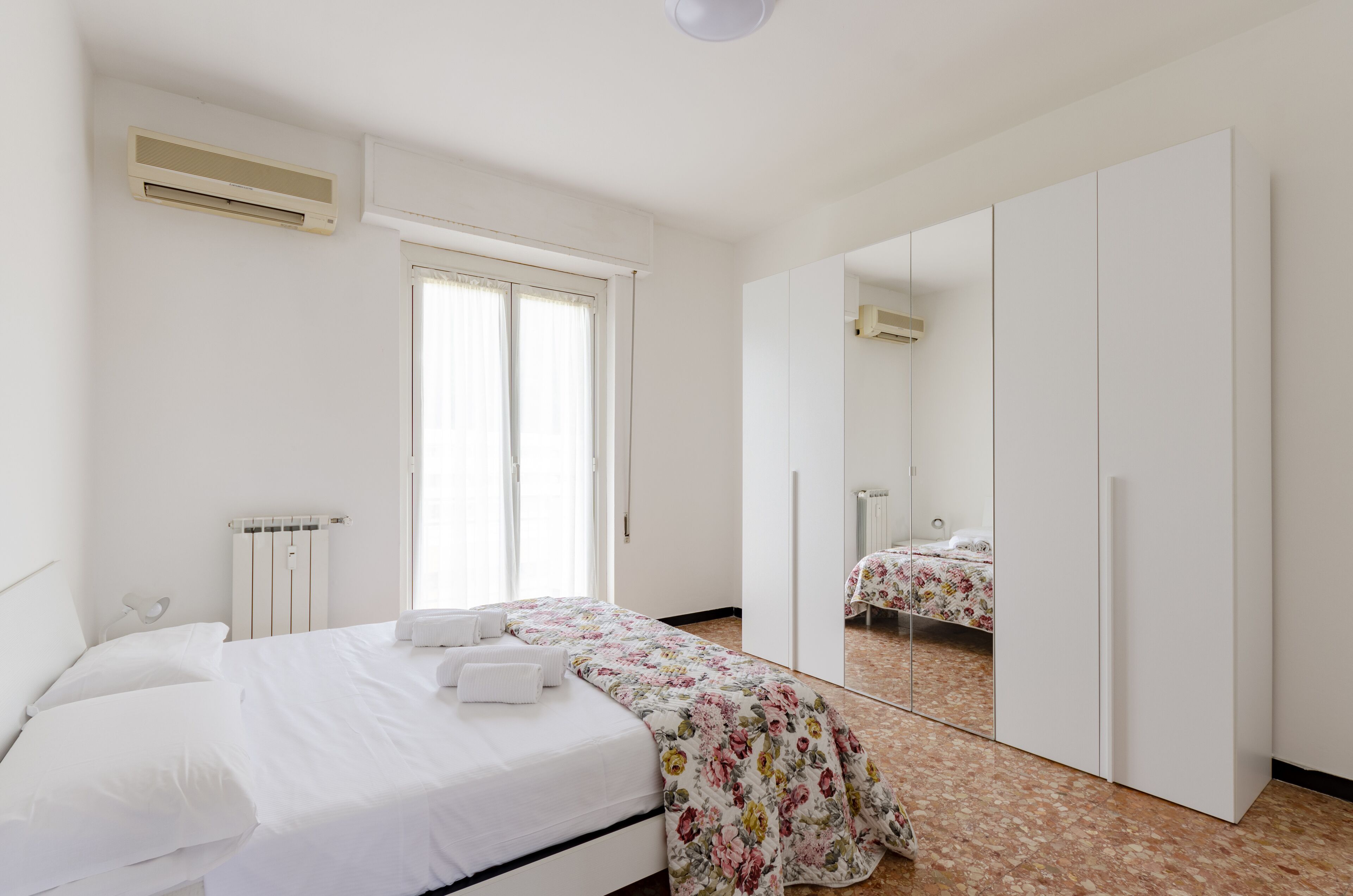 A bedroom with a bed, a radiator, a window, and a wardrobe.