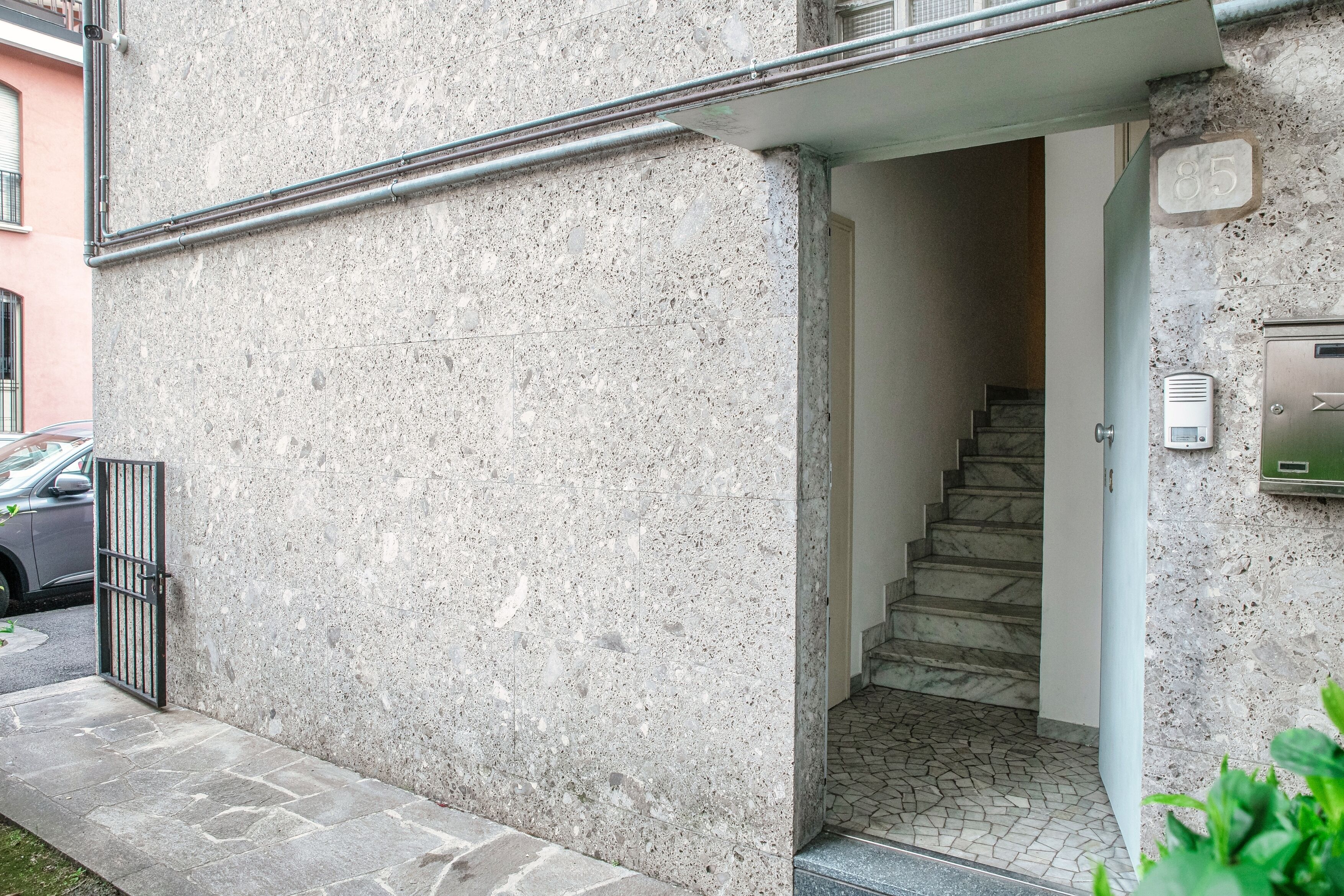 A building entrance with a stone facade, a metal gate, a staircase leading inside, and a mailbox on the right.