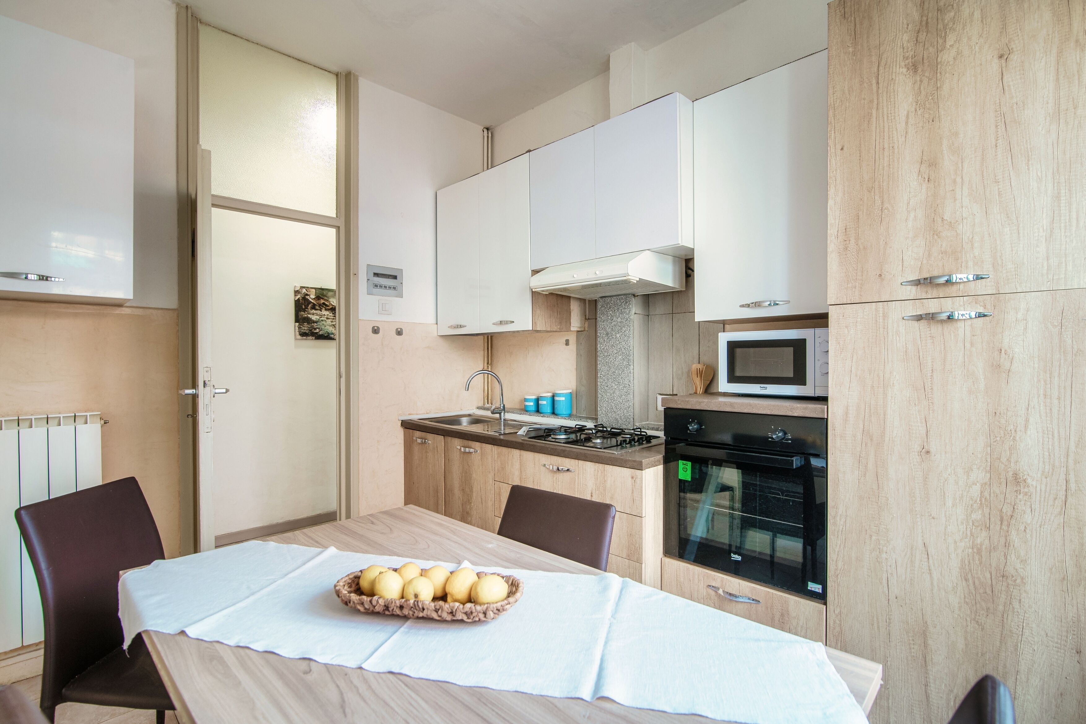 A modern kitchen with white cabinets, a microwave, a stove, and a dining table with a basket of potatoes.