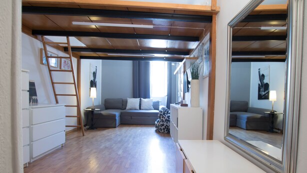 A modern living room with a wooden ceiling, a sofa set, a white cabinet, and a large mirror.