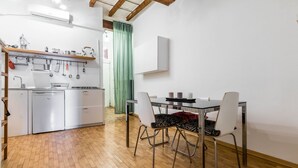 A compact kitchen with a dining area, wooden flooring, and a green curtain.