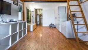 A spacious room with a wooden floor, white shelving units, a television mounted on the wall, and a ladder leaning against the wall.