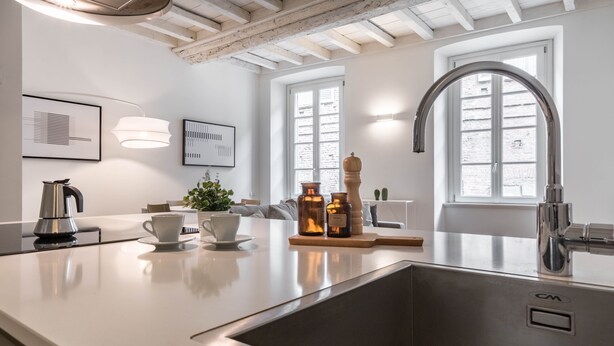 A modern kitchen with a stainless steel sink, white countertops, and a window with a view of the city.