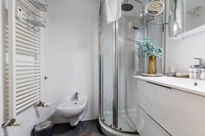A modern bathroom with a glass-enclosed shower, a white sink, and a bidet. - JOIVY Modern Studio Near City Centre (Milan)