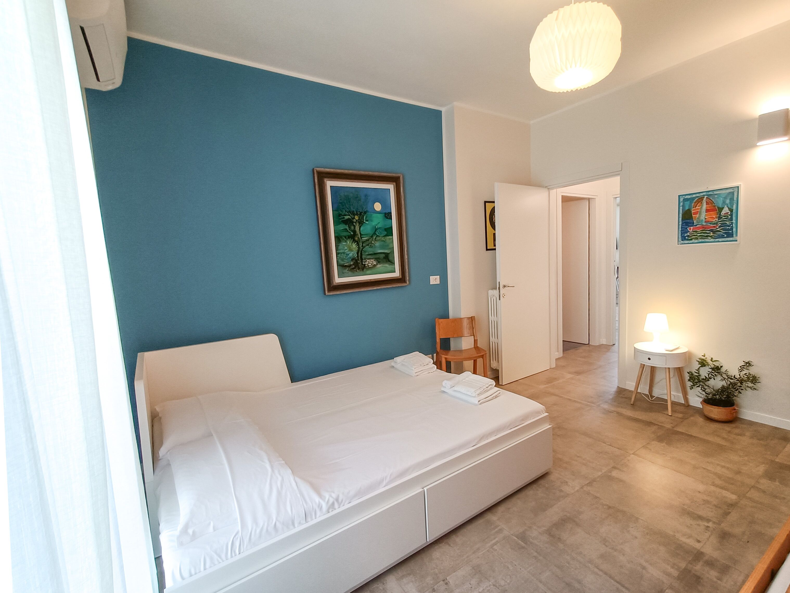 A bedroom with a bed, a chair, a bedside table with a lamp, and a framed picture on the wall.