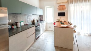 A modern kitchen with a central island, stainless steel appliances, and a dining area with a table and chairs. - JOIVY Bright Flat W/2 Balconies & Sea View (Alassio)