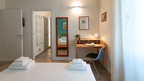 A hotel room with a bed, a desk with a chair, a mirror, and a wall-mounted air conditioner. - JOIVY Bright Flat W/2 Balconies & Sea View (Alassio)