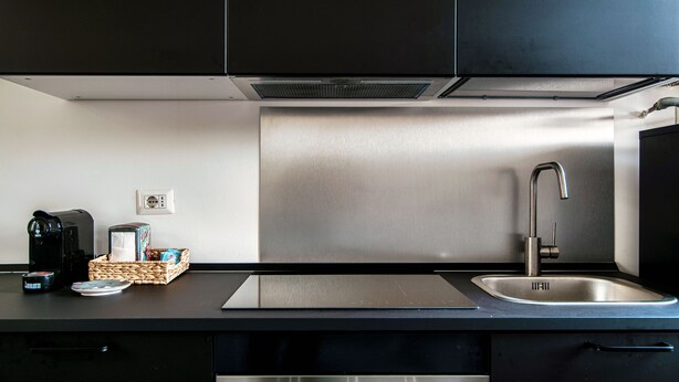 A modern kitchen with black cabinets, a stainless steel sink, and a built-in stove. - JOIVY Stylish Flat, 5-Minute Metro Trip To Centre (Milan)