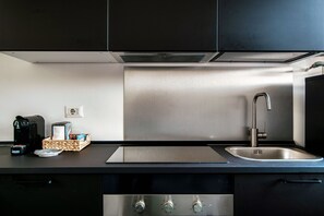 A modern kitchen with black cabinets, a stainless steel sink, and a built-in stove. - JOIVY Stylish Flat, 5-Minute Metro Trip To Centre (Milan)