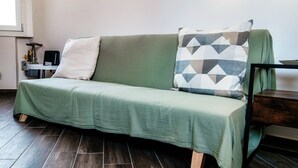 A green sofa with a white and geometric patterned pillow, a small table with a speaker, and a wooden floor. - JOIVY Stylish Flat, 5-Minute Metro Trip To Centre (Milan)