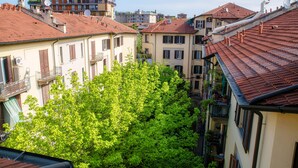 A residential area with multi-story buildings, balconies, and a dense green tree in the foreground. - JOIVY Stylish Flat, 5-Minute Metro Trip To Centre (Milan)