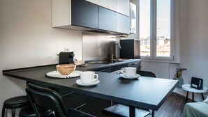 A modern kitchen with a dining area, featuring a black countertop, white cabinets, and a view through a window. - JOIVY Stylish Flat, 5-Minute Metro Trip To Centre (Milan)